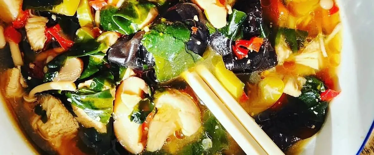 A bowl of clear broth with mushrooms, leafy greens and chilli