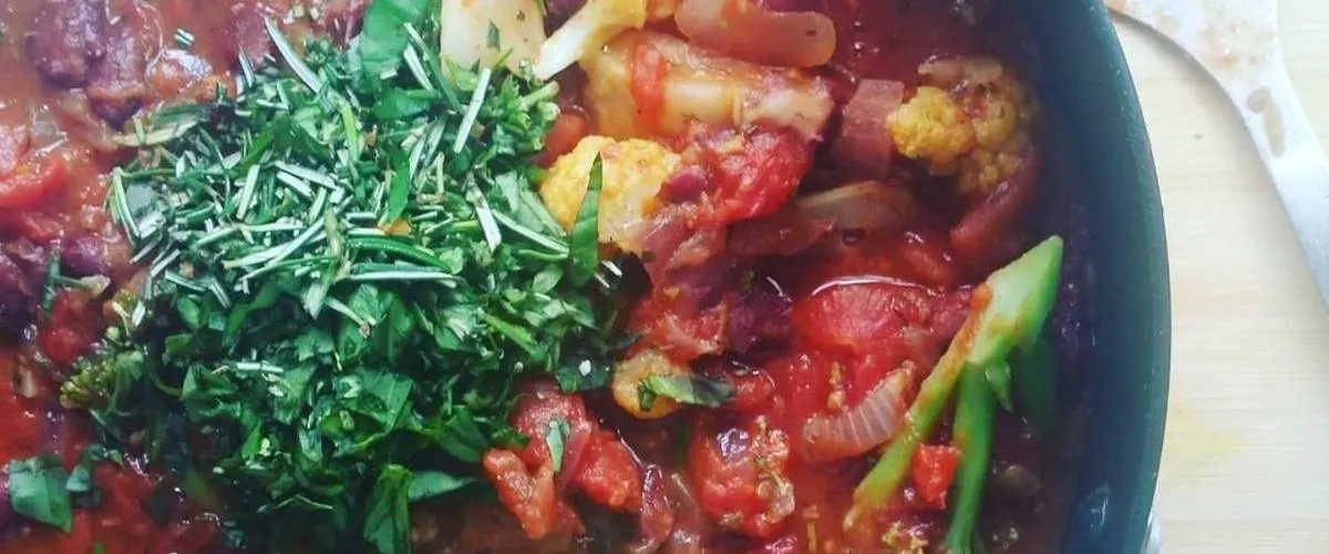 A pan of slow cooked vegetables in tomato, topped with fresh chopped herbs