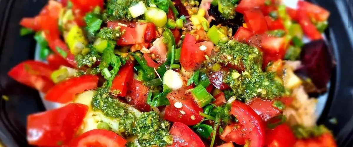 A bowl of chopped tomato, herbs, spring onion and green pesto